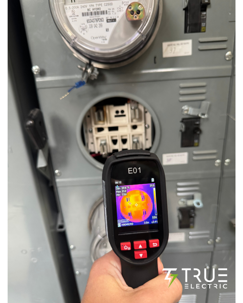 A licensed technician using a handheld infrared camera to perform an electrical thermal imaging scan on a building breaker panel.