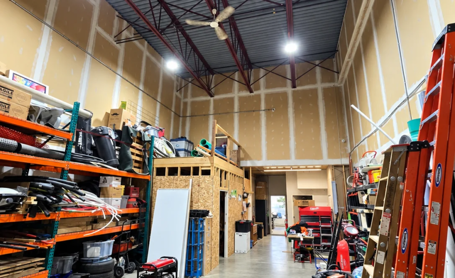 High-visibility linear aisle lighting and LED high bays illuminating narrow racking corridors inside a South Surrey commercial fulfillment warehouse.
