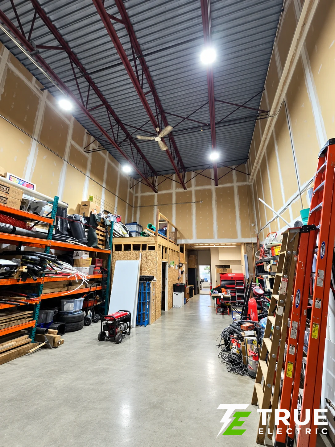 High-visibility linear aisle lighting and LED high bays illuminating narrow racking corridors inside a South Surrey commercial fulfillment warehouse.